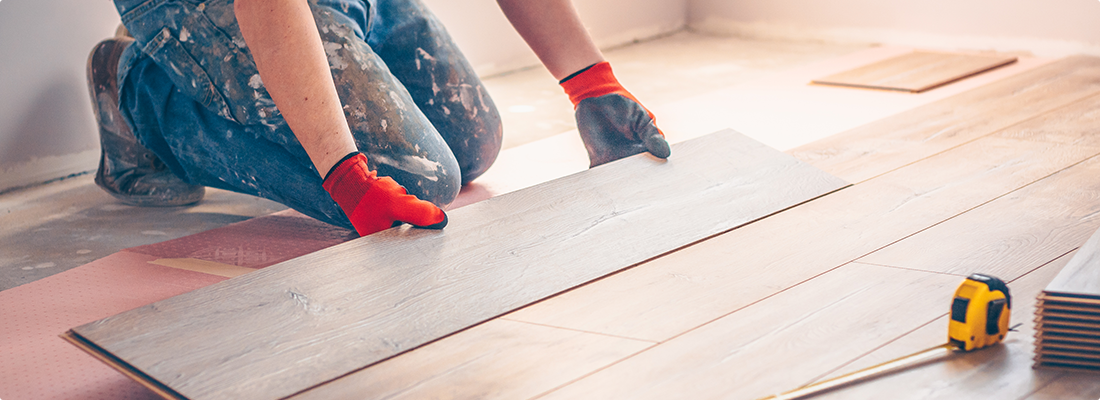 Man installing hardwood flooring with glove and tape measure