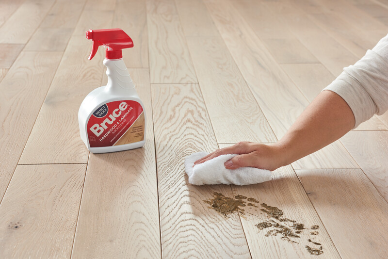 Woman wiping a spill from a hardwood floor using Bruce Hardwood and Laminate Cleaner
