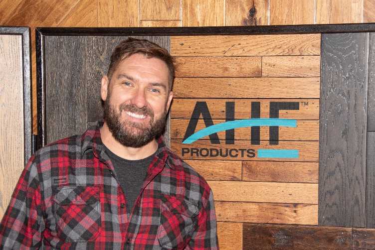 Mark Bowe in front of an AHF Products sign for the Barnwood Loving collection of barnwood flooring