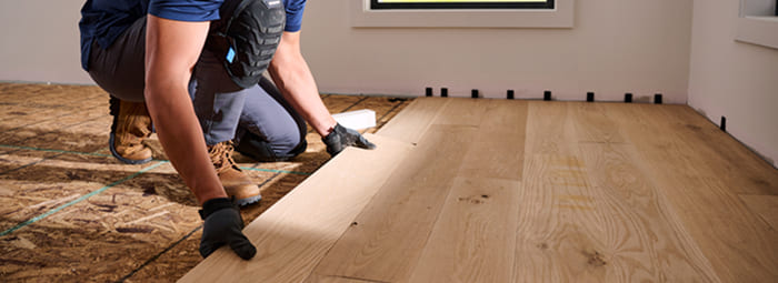 Installer placing wide plank unfinished hardwood flooring during installation.