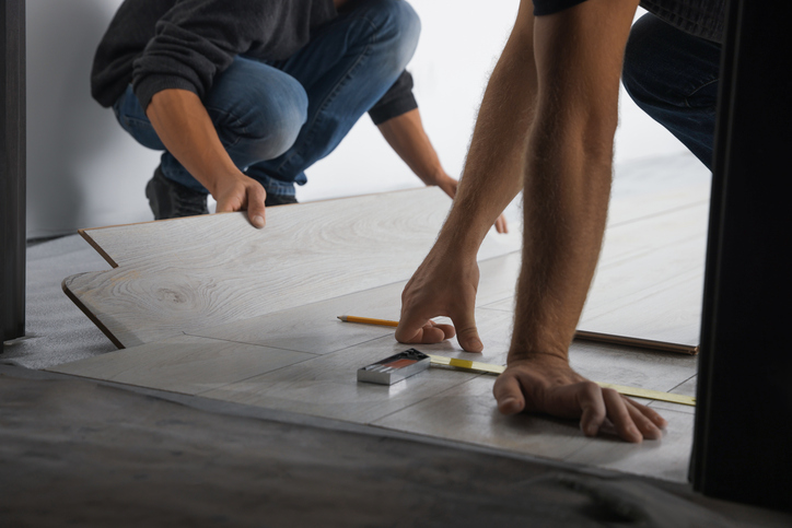 Two people installing a floating floor with one measuring and the other clicking a plank into place
