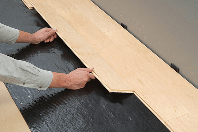 man's hands locking a piece of hardwood flooring into the grooves of another hardwood plank