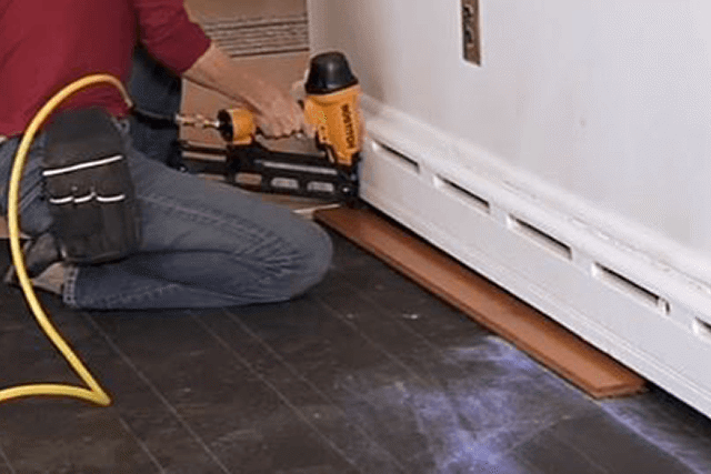 Hardwood installer on his knees with a goal and laying hardwood floors 