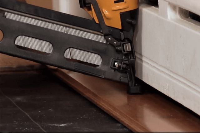 Close up of a nail gun being used to lay hardwood flooring