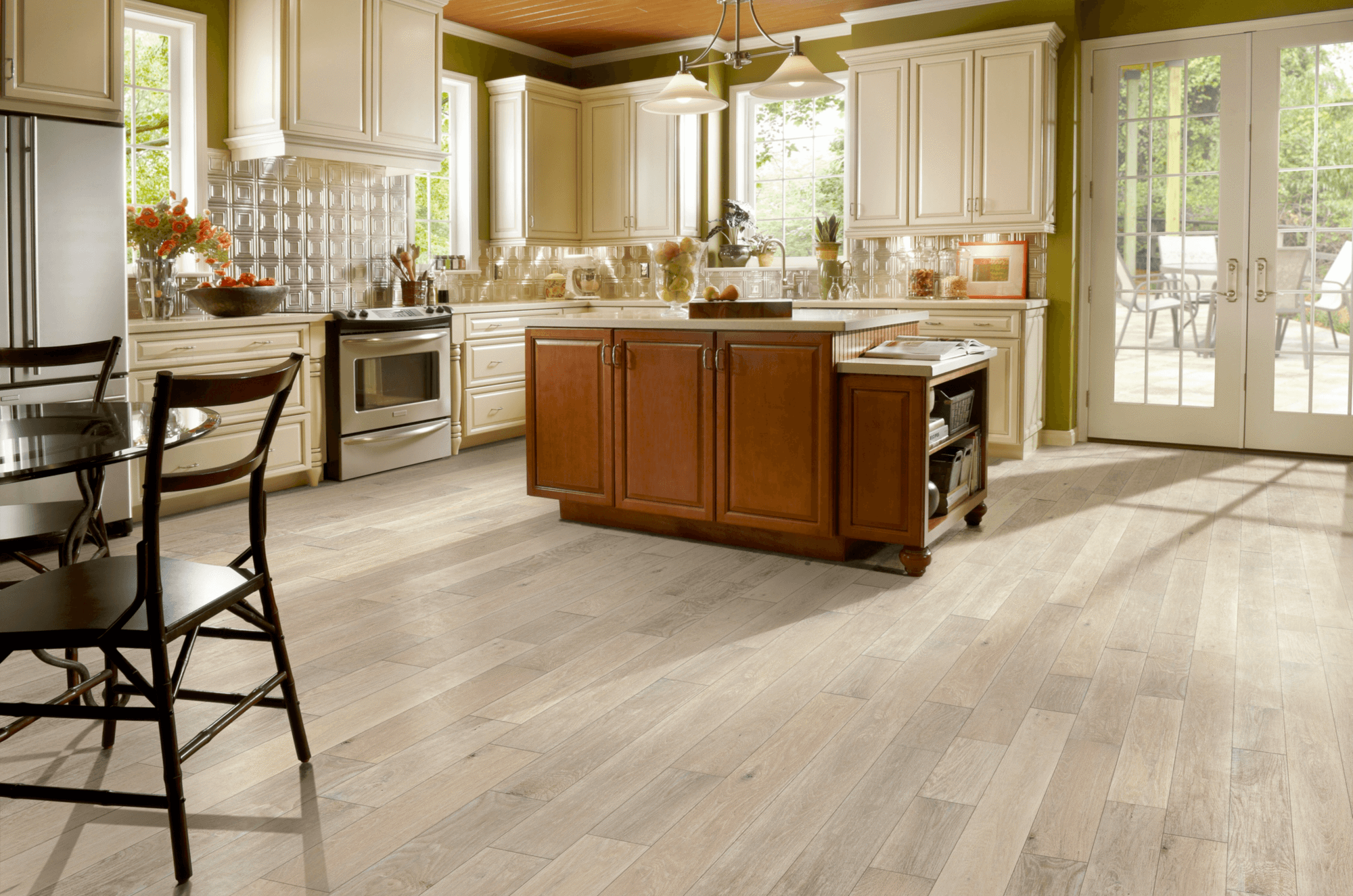 Large early American kitchen with an island and French doors overlooking a patio presenting hand-scraped oak hardwood flooring